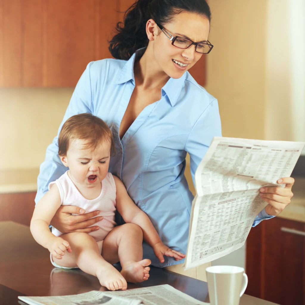 Woman reading a newspaper while holding a baby in a home setting