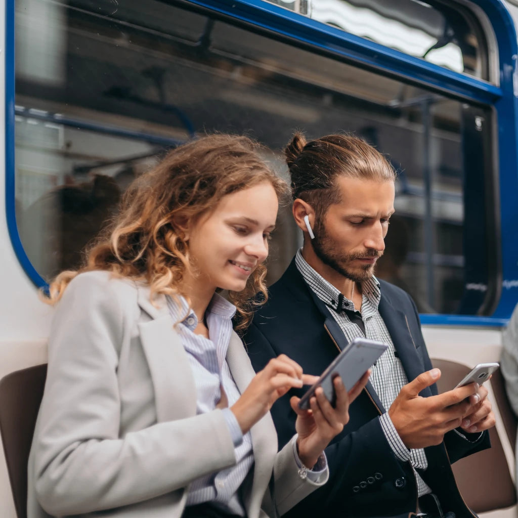 Two people sitting on a train, using their smartphones.
