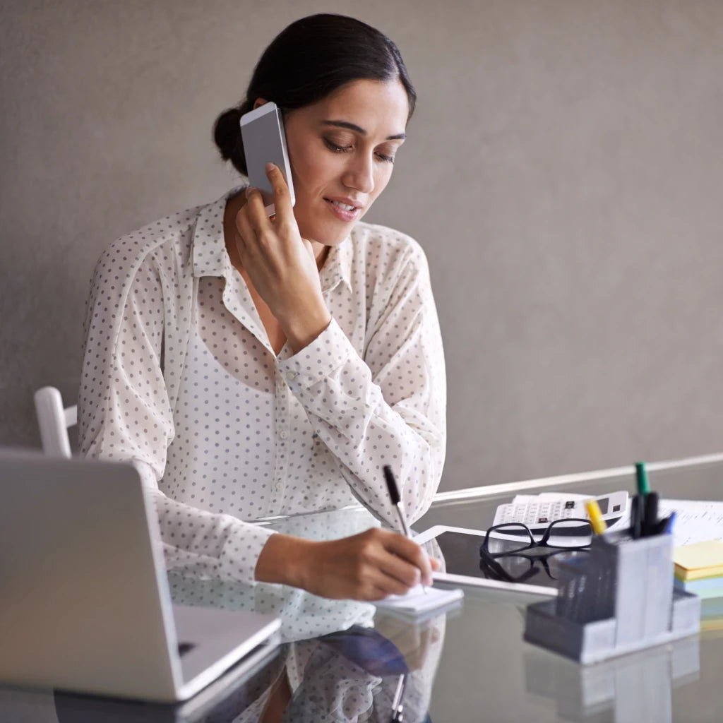 Woman on phone at a desk with laptop and office supplies
