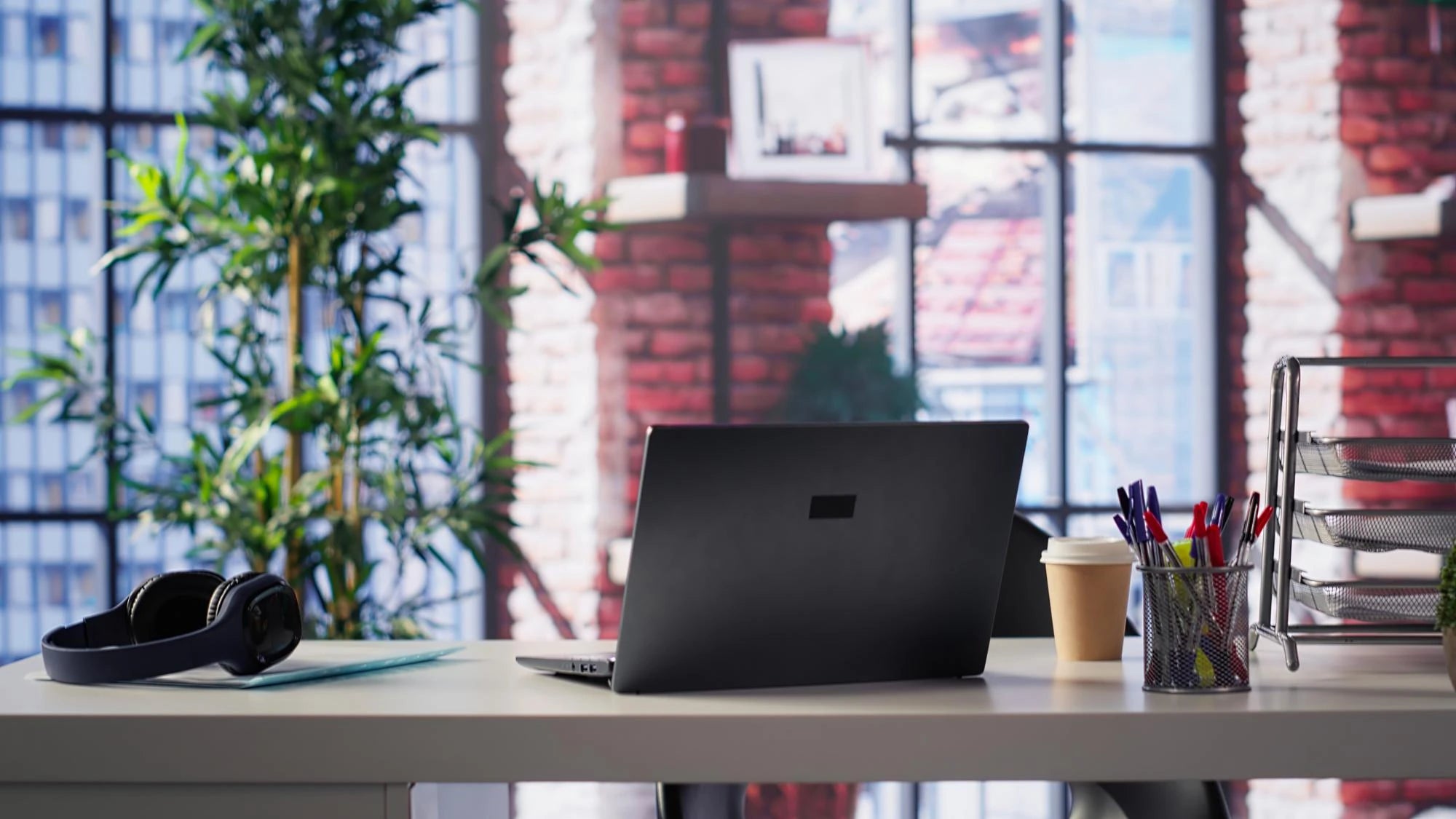 Laptop on a desk with a coffee cup and stationery in an office setting