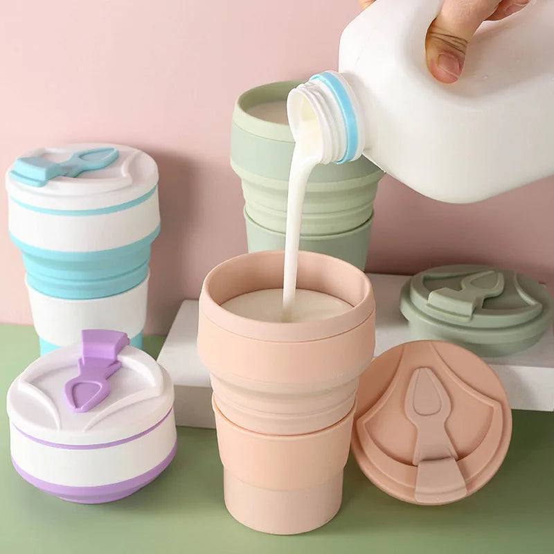 Collapsible silicone cups with various colors and lids on a green surface, with a pink background.
