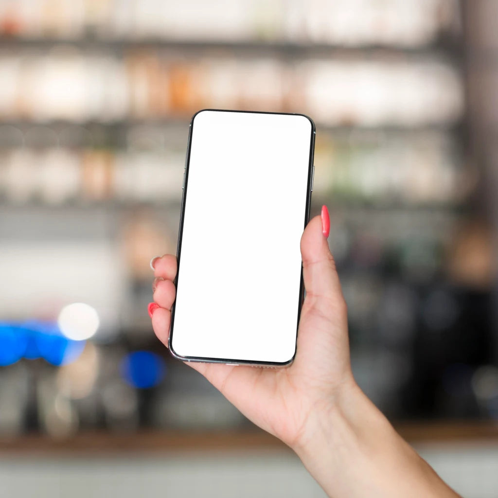 Hand holding a smartphone with a white screen against a blurred indoor background