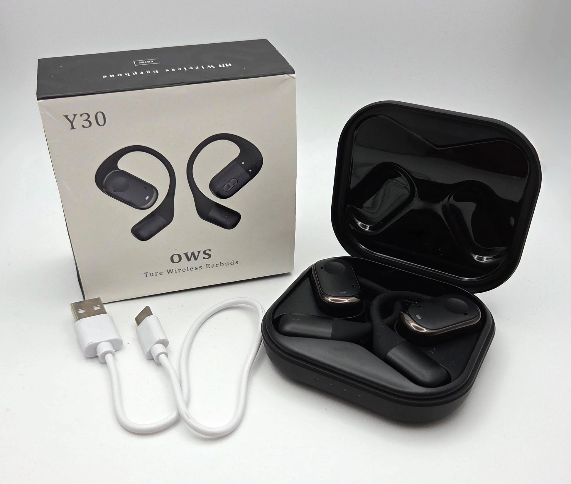 Black wireless earbuds in a case with packaging, USB cable, and charging adapter on a gray background.
