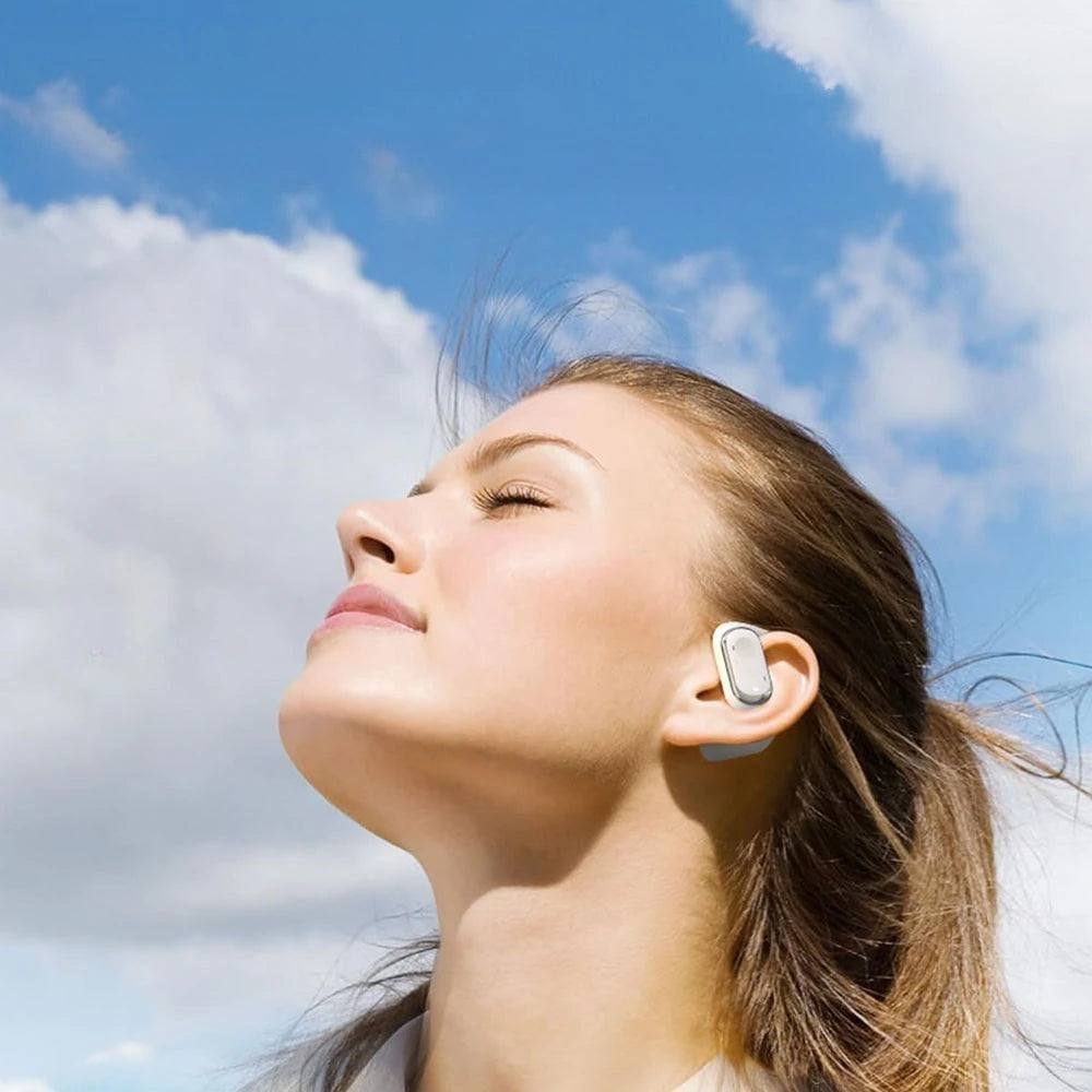 Woman wearing an open-ear earbud with a blue sky background