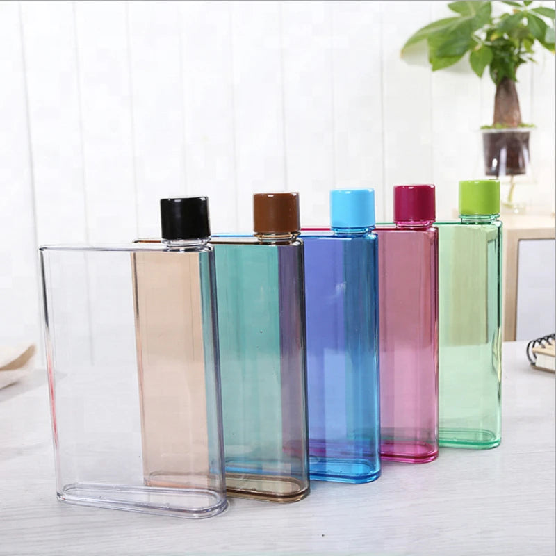 Set of colorful transparent bottles with caps on a light wooden surface.