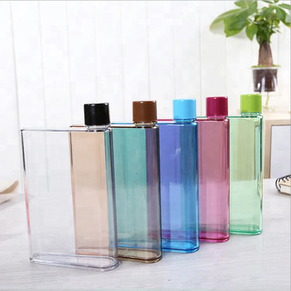 Set of colorful transparent bottles with caps on a light wooden surface.