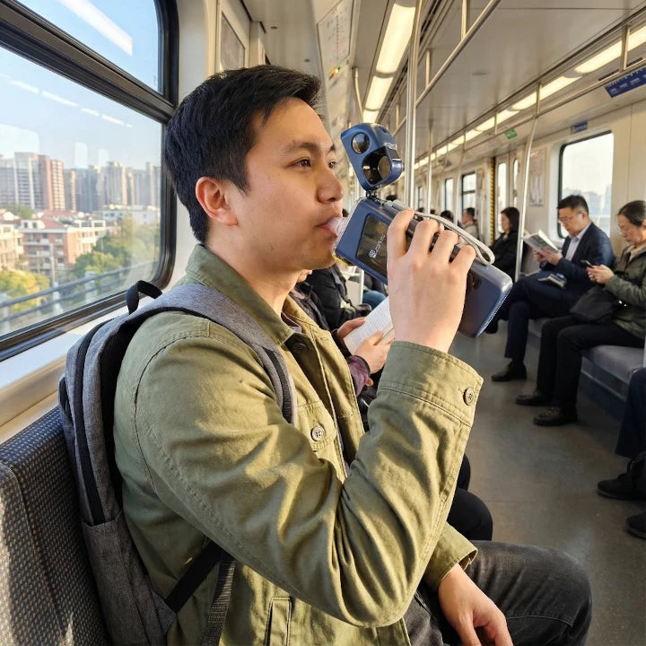 Everyday commuter holding and drinking from the rectangular sports water bottle on a public rail.