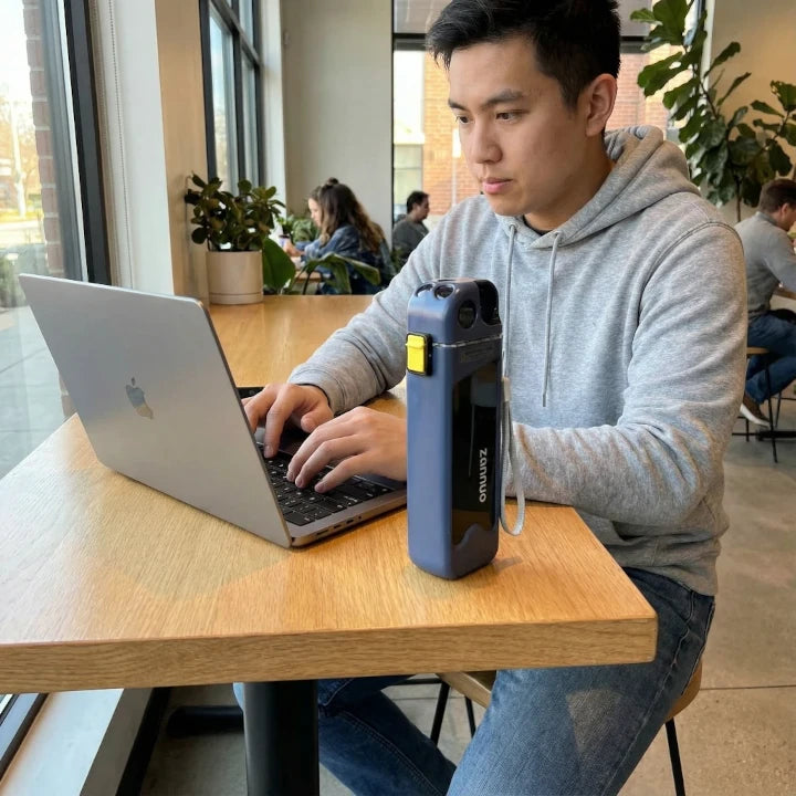 Person using a laptop with a rectangular sports bottle on a table in a casual setting