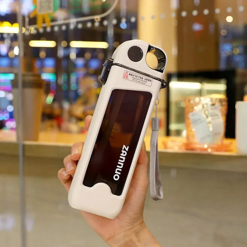 Hand holding a white square water bottle in an indoor setting.