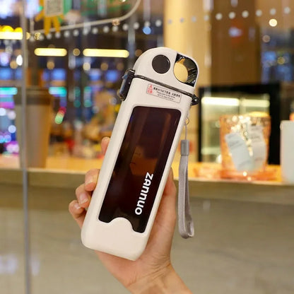 Hand holding a white square water bottle in an indoor setting.