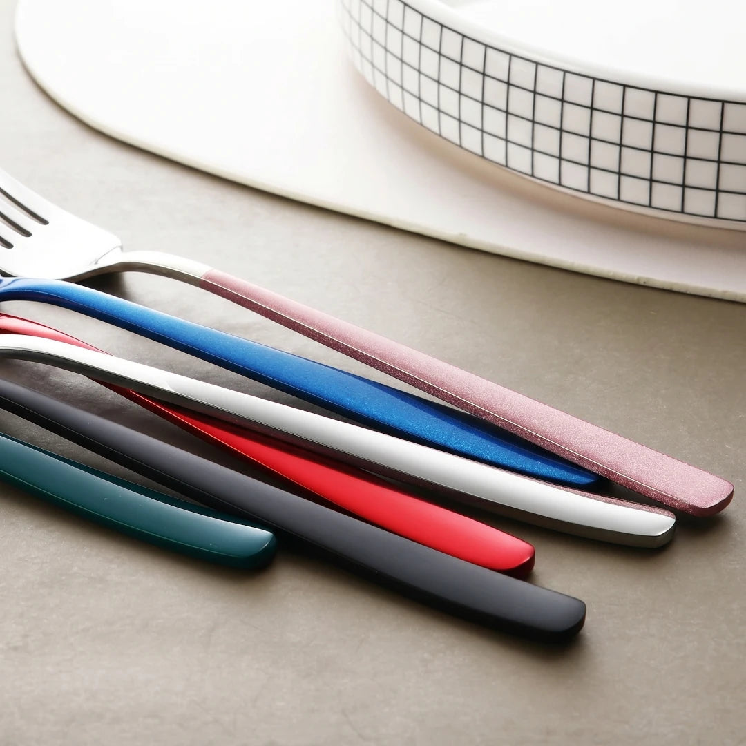 Close up of a set of colorful utensil handles on a neutral surface with a grid-patterned plate in the background.