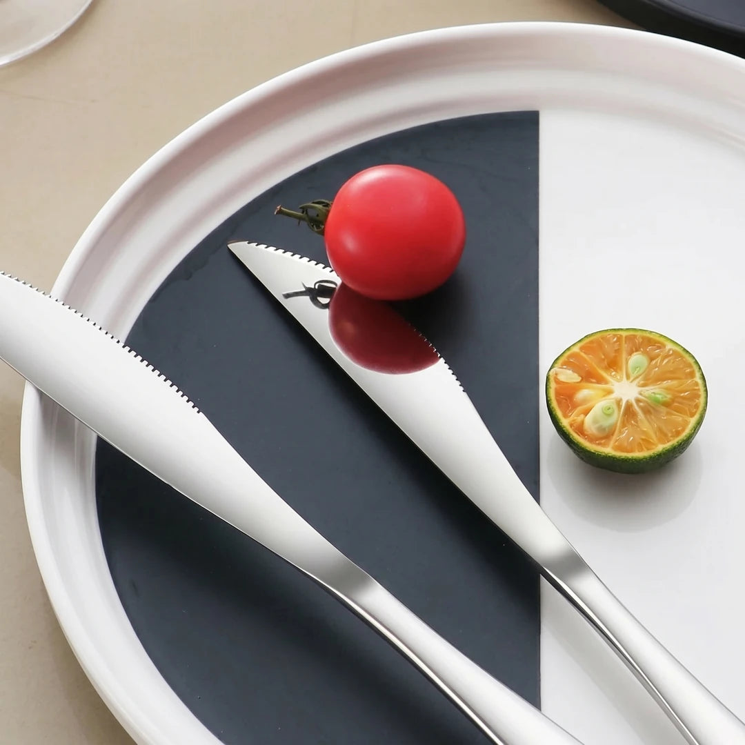 2 304 Stainless steel knife reflecting a tomato with an orange half on a plate