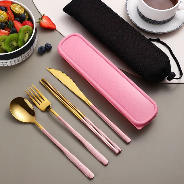 Pink and gold cutlery set with a pink case on a gray surface, next to a bowl of fruit and a cup.