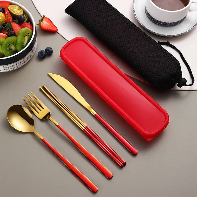 Red and gold cutlery set with a red case on a gray surface, next to a bowl of fruit and a cup.