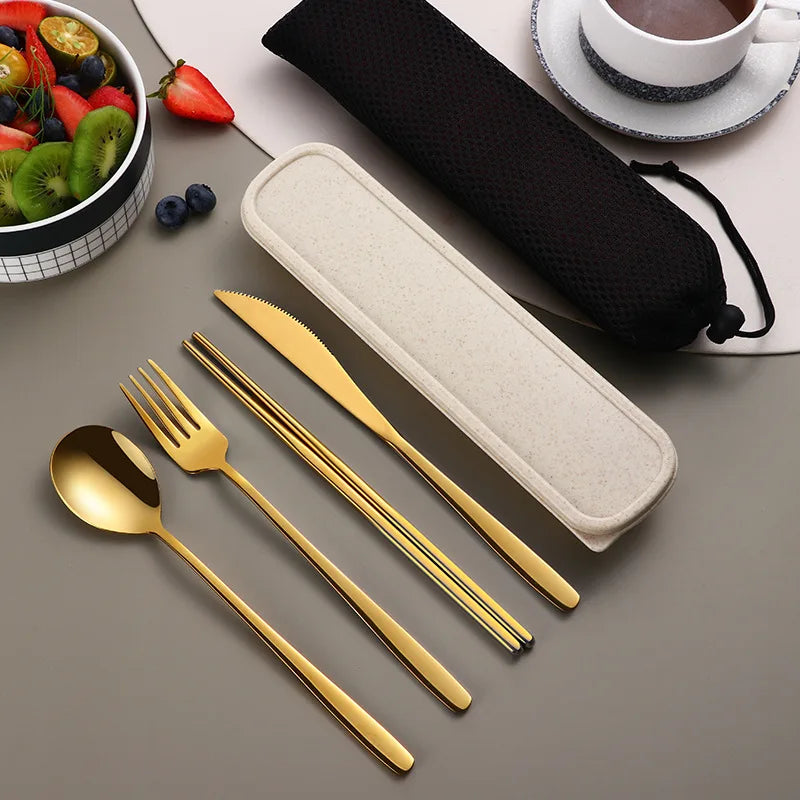 Gold cutlery set with case on a gray surface, next to a bowl of fruit and a cup of coffee.