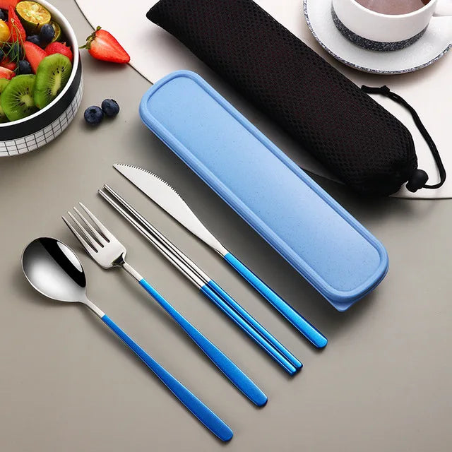 Set of silver cutlery with blue handles in a blue case on a table with fruits and a cup.