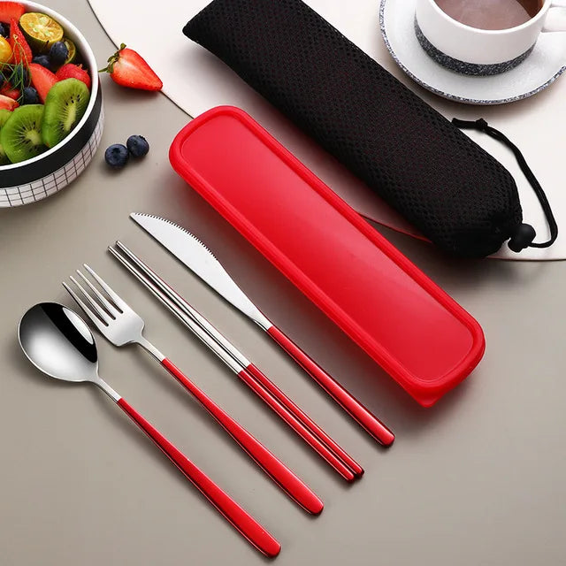Red and silver cutlery set with a red case on a table with fruit and a cup.