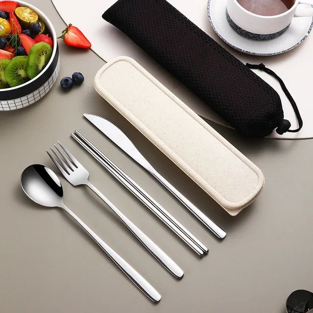 Set of silver cutlery with a case on a table with fruits and a cup.